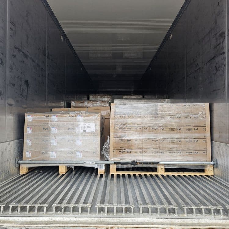 Two shrink-wrapped pallets of boxes on wooden pallets, secured with a load bar inside a truck trailer.
